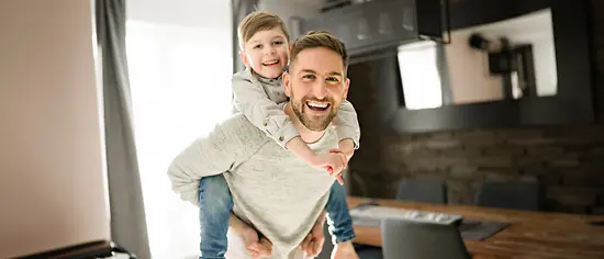 Private Krankenversicherung für Angestellte mit einem jungen Vater, der seinen Sohn auf dem Rücken trägt.