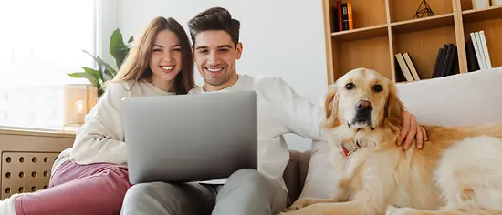 Ein junges Paar sitzt mit einem Hund auf dem Sofa und vergleicht die besten Hundekrankenversicherungen.